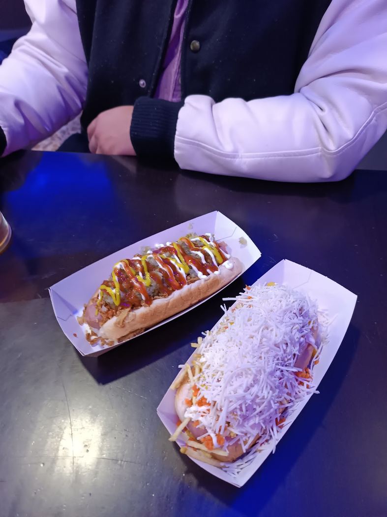 Dos hot dogs: uno clásico con mostaza y cebolla, y otro con queso rallado.